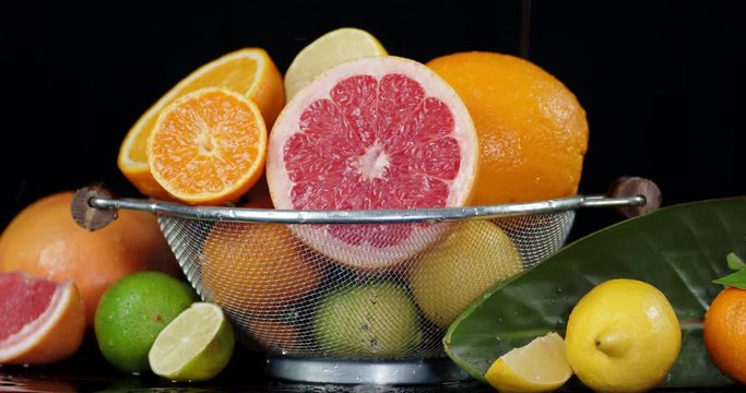 Various citrus fruits in a colander with leaves falling drops of water.