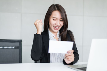Young beautiful Asian business woman feeling happy or success after look at bonus money or salary in an envelop.