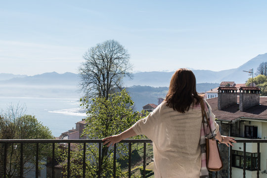 Brunette Woman With Long Hair Leaning Out On The Balcony