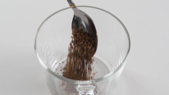Spoon with instant coffee puor in a white mug on a black background. Slow motion.