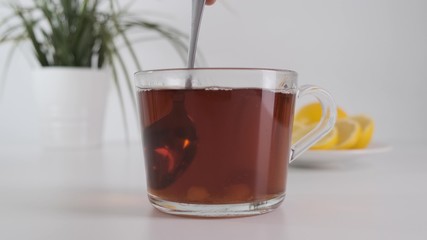 Close up stirring sugar with metal spoon in transparent glass cup tea on white table. Slow motion.