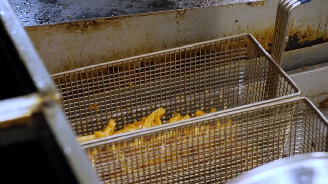 Chef is tossing deep fryer above the hot oil. Close up video as chef takes the deep fryer and tosses it.