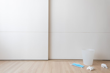 The trash with secondhand white tissue papers and a blue surgical face mask placed on the floor with copy space.