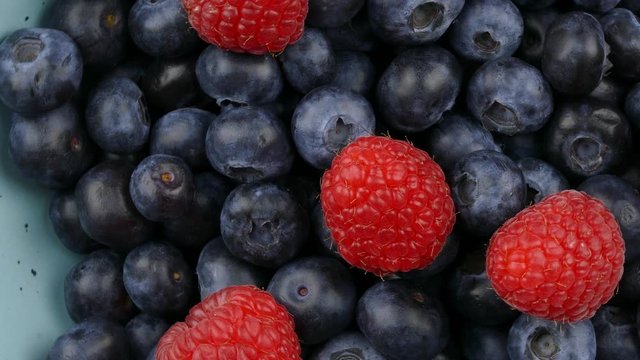 fresh blueberry and raspberry fruits in a blue bowl rotating top view closeup 4k