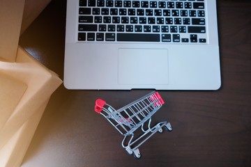 A small red shopping cart on black table with a lot of parcel or box brown paper wrapped. Concept...