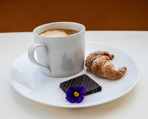 A cup of coffee, croissant and dark chocolate on the white table.