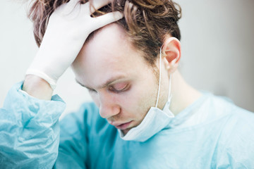 tired and sad doctor surgeon in depression is upset and holds his head. Medical error and...