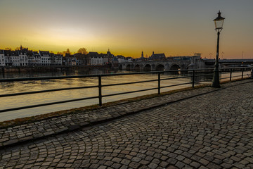 Naklejka na ściany i meble View on the skyline of Maastricht during sunset seen from the Wyck neighbourhoud with a view on the typical cobbelstone streets, river Meuse and the old roman bridge
