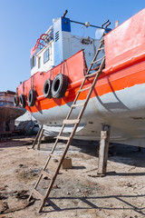 Old rusty orange vessel under repair located on grungy dry dock in shipyard against blue sky on...