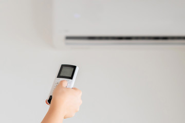 Brunette woman holding remote controller from air conditioner inside the room. Back view.