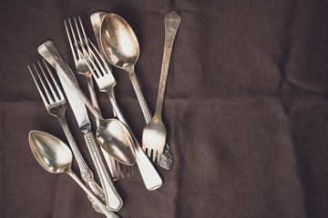 Metal vintage cutlery on a dark linen napkin in a row. Flat lay, top view.