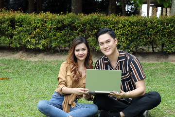 Young Asian Malay man woman outdoor green park sit on grass use study discuss laptop look at camera