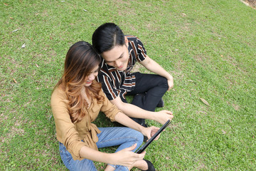 Young Asian Malay man woman outdoor green park sit on grass use study discuss tab