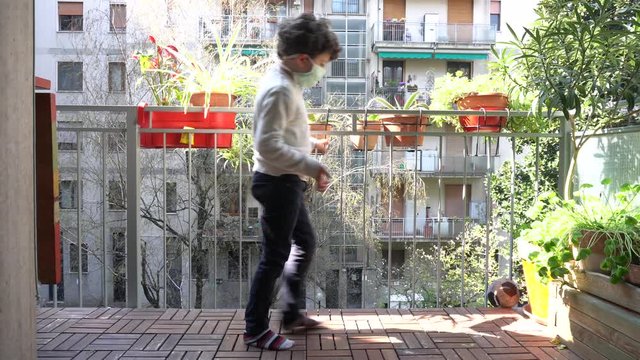 Europe, Italy , Milan - children boy  five years with mask at home during quarantine due n-cov19 Coronavirus outbreak - life stile in apartment - playing alone soccer football on the balcony