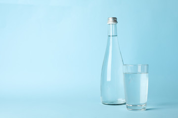 Glass and bottle with water on blue background, space for text