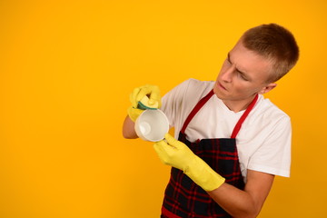 serious man in an apron washes a cup in rubber glove on a yellow background