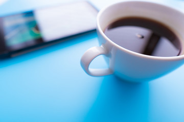 Digital tablet computer and cup of coffee on blue backgroubnd. Simple workspace or coffee break with web surfing.