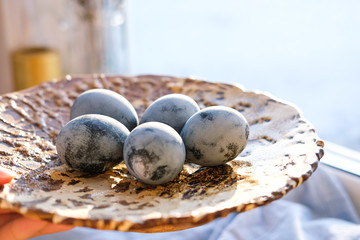 Blue Easter eggs lie on a handmade ceramic plate on the windowsill. Rustic style, natural materials and textiles