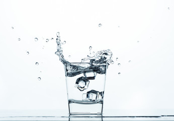 Ice cubes falling in a glass of water, splashing around. On light background.