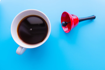 Blue background and bell. In another corner of the picture is a white cup of coffee. Concept - coffee break, time to drink coffee