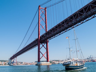 sailing yacht passing the Bridge of the 25 th of April, over the river Tejo in Lisbon, Portugal