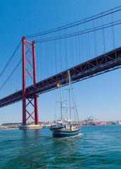 sailing yacht passing the Bridge of the 25 th of April, over the river Tejo in Lisbon, Portugal