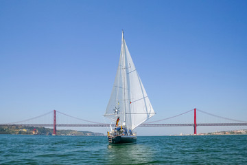 sailing yacht passing the Bridge of the 25 th of April, over the river Tejo in Lisbon, Portugal