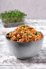Pilaf with meat in a ceramic bowl on the white wooden table. Traditional oriental cuisine meal
