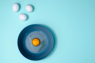 Three white eggs and a blue plate with broken egg on the table on the mint blue background