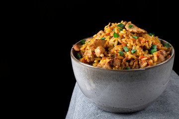 Pilaf with meat in a ceramic bowl on the edge of the table against the black background. Traditional oriental cuisine meal. Low key photo