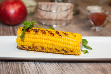 baked corn on a black plate with green branches on a wooden table