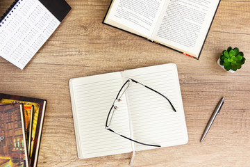 Work space education concept on vintage wooden table desk with glass on open book, blank, notepad and stack of book , glass, green plant and flat lay.