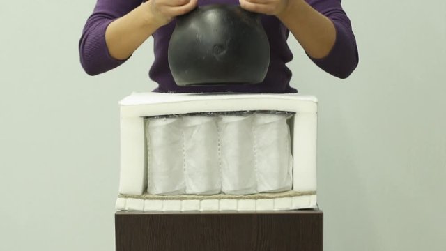 Woman hands puts a heavy weight on an orthopedic foam mattress slow motion