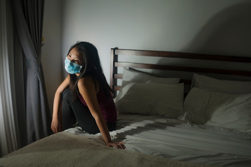 Naklejka premium covid-19 quarantine and home lockdown - young beautiful scared and overwhelmed Asian Chinese woman in protective mask feeling worried about coronavirus pandemic