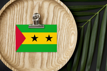 Sao Tome And Principe flag tagged on wooden plate. Tropical palm leaves monstera on background....