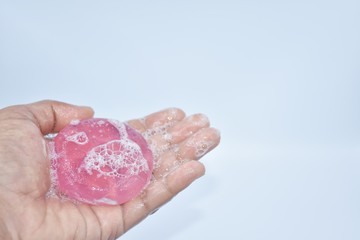 The hand holding a purple soap that is wet and has a bubble on a white  background