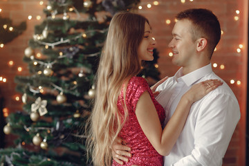 Couple near christmas tree. Lady in a pink dress. Man in a white shirt.