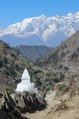 View of typical white stone tibetan buddhist stupa in Himalayas next to mani sones on footpath to...