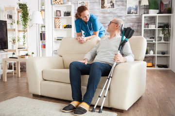 Old man sitting on couch holding his crutches