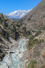 Beautiful mountain valley with flowing river in Himalayas in the morning. Taboche mountain in the background. Several bridges over the river. Mountainside is covered by trees. Beautiful landscape. 
