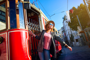 Beautiful young girl tourist in a hat poses in front of Taksim tram at popular Istiklal street in...