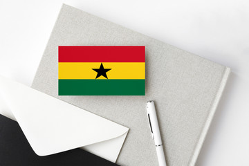 Ghana flag on minimalist letter background. National invitation envelope with white pen and notebook. Communication concept.