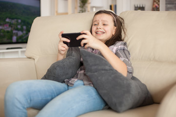 Cheerful little girl playing video games on smartphone