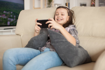 Obraz premium Cheerful little girl playing video games on smartphone