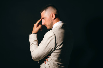 Dramatic portrait of business man in profile with hand near his face on black background.