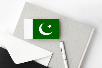 Pakistan flag on minimalist letter background. National invitation envelope with white pen and notebook. Communication concept.