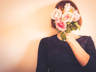 Young woman holding bouquet of pink flowers covering her face. Faceless female portrait