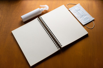 epidemic healthcare concept ,Alcohol spray and face mask with paper notebook on wooden background with copy space