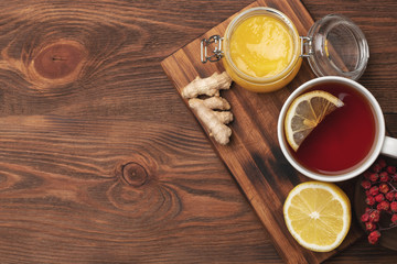 Fototapeta na wymiar flat lay of natural ingredients for tea to increase immuntiy during self-isolation period. lemon on a wooden plate, ginger, hot tea and honey in a wooden spoon.
