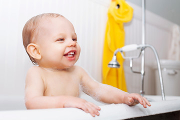 Portrait of cheerful baby boy sitting in bathtub